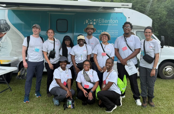 A group of people in matching shirts pose in front of a mobile health clinic parked on grass.