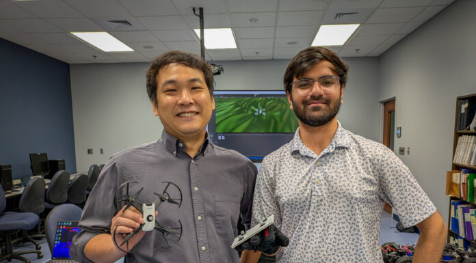 Engineering research project combines virtual reality and the real world Dr. Hunmin Kim and Shrey Patel in a lab. Dr. Kim holds a drone, and Patel wears a glove with probes affixed to it.