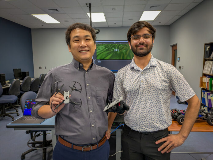 Dr. Hunmin Kim and Shrey Patel in a lab. Dr. Kim holds a drone, and Patel wears a glove with probes affixed to it.