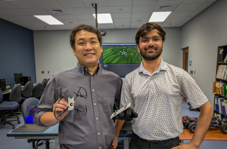 Dr. Hunmin Kim and Shrey Patel in a lab. Dr. Kim holds a drone, and Patel wears a glove with probes affixed to it.