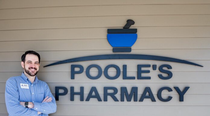 Alumnus continues legacy of community pharmacy Dr. Thomas Sherrer stands smiling with arms crossed next to a sign reading Poole's Pharmacy on an exterior wall.