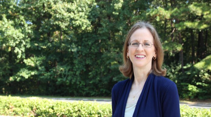 Pharmacy’s Dr. Candace Barnett announces retirement after four decades of service A woman with glasses stands outdoors in a parking lot, smiling, with trees and greenery in the background.
