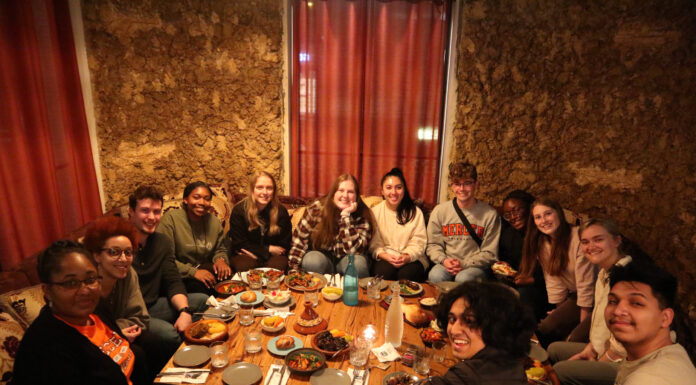 Mercer professors publish book about impact of study abroad on students A group of people sit around a low table, sharing a meal in a warmly lit restaurant with earthen walls.