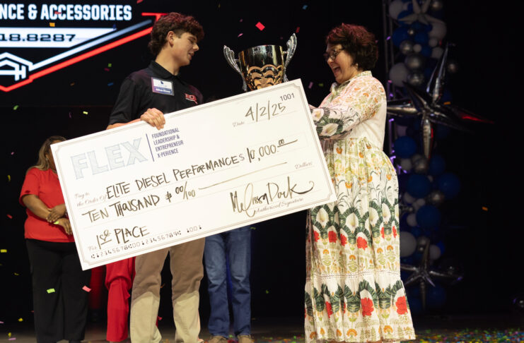 A young man receives a trophy and a $10,000 check for first place at an event, standing beside a woman on stage.