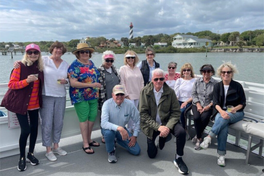 A group of people pose near the water, with a lighthouse visible in the background.