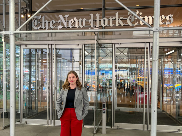 Rylee Kirk stands in front of The New York Times building entrance.