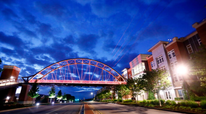 Engineering school to teach sustainability in core classes starting this fall A lit pedestrian bridge spans across an empty street between modern buildings at dusk under a cloudy blue sky.