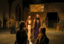 Mercer Theatre announces 2025-26 season: Bold productions take the stage Actors in a dramatic stage scene stand under warm lighting, with a woman in purple at the center and others in muted costumes.