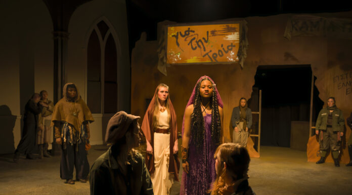 Mercer Theatre announces 2025-26 season: Bold productions take the stage Actors in a dramatic stage scene stand under warm lighting, with a woman in purple at the center and others in muted costumes.