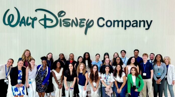 Senior gains media experience, connections during NYC internship A large group of people pose and smile in front of a wall with the Walt Disney Company logo.