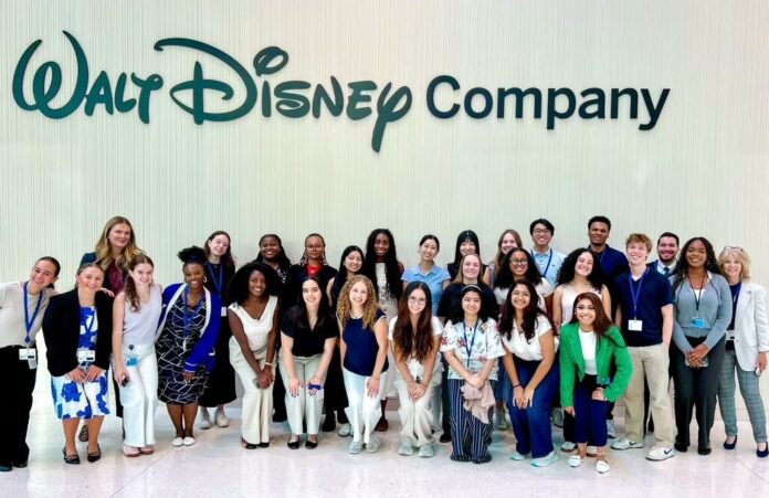 A large group of people pose and smile in front of a wall with the Walt Disney Company logo.