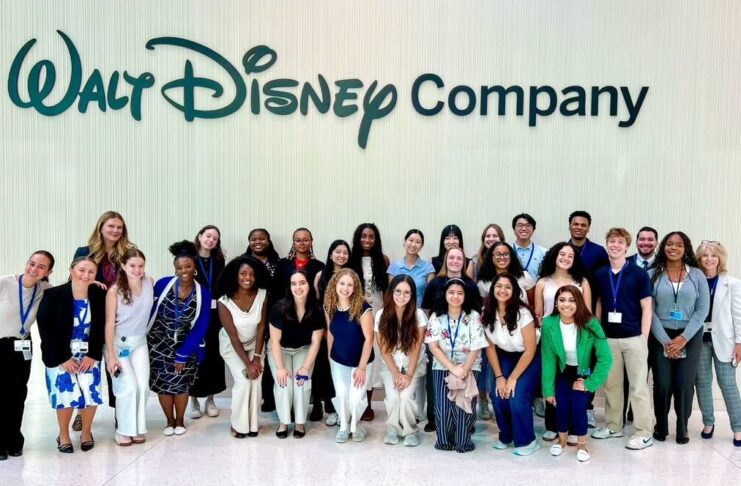 A large group of people pose and smile in front of a wall with the Walt Disney Company logo.