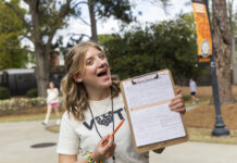 At Mercer, student civic engagement is tradition A person outdoors holds a clipboard with a form, smiling and pointing at it with an orange pen.