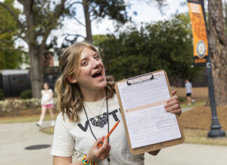 Recent grad selected for ALL IN Campus Democracy Challenge’s 2026 Student Voting Honor Roll A person outdoors holds a clipboard with a form, smiling and pointing at it with an orange pen.