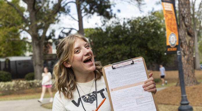 At Mercer, student civic engagement is tradition A person outdoors holds a clipboard with a form, smiling and pointing at it with an orange pen.