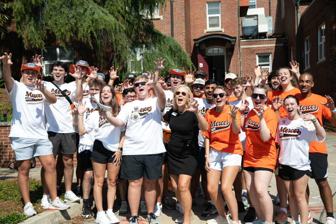 A group of students and an adult stand outside, smiling and making paw gestures in matching Mercer shirts.