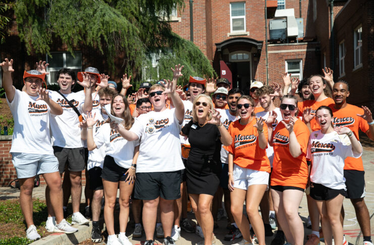 A group of students and an adult stand outside, smiling and making paw gestures in matching Mercer shirts.