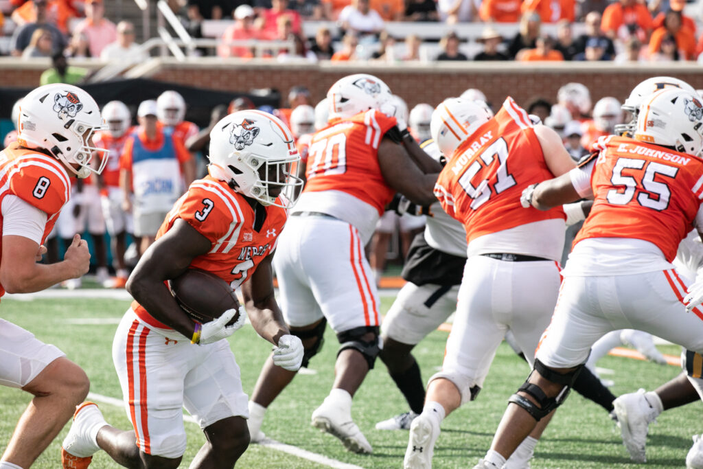 A Mercer football player runs with the ball while teammates block.
