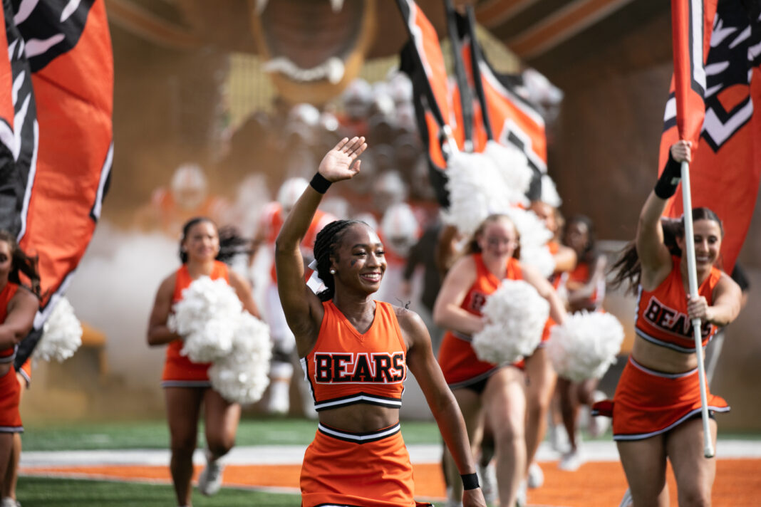 Mercer cheerleaders wave and carry flags on a football field.