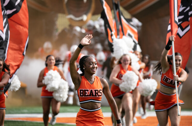 Mercer cheerleaders wave and carry flags on a football field.