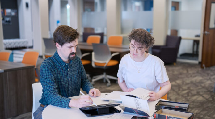 Humanities research projects explore the Holocaust, life’s meaning, games, film Two people sit at a round table in an office, reading books and taking notes together.