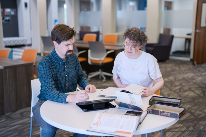 Two people sit at a round table in an office, reading books and taking notes together.