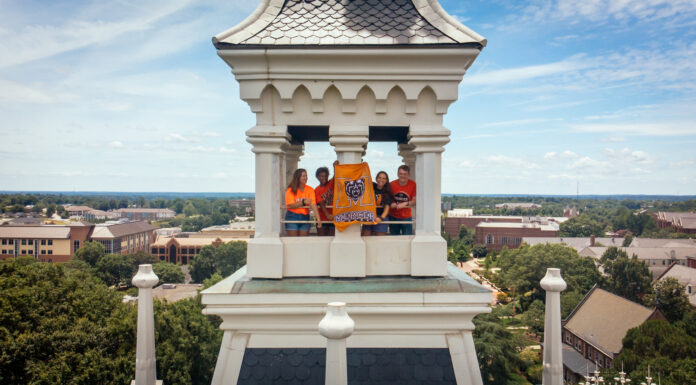 Mercer one of Princeton Review’s ‘Best Colleges’ for 23rd consecutive year Four people stand in a white clocktower holding a Mercer University flag, with campus buildings visible below.
