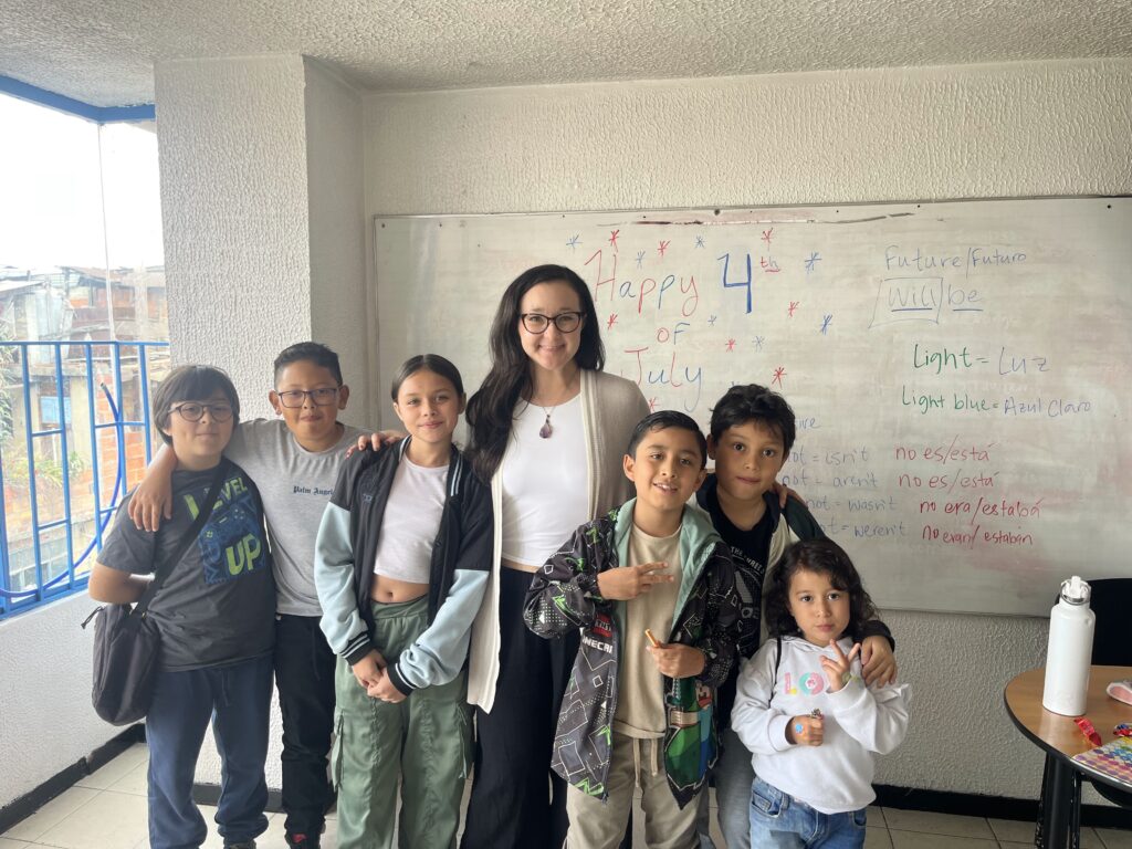 A teacher stands with six students in front of a whiteboard decorated for the 4th of July in a classroom.