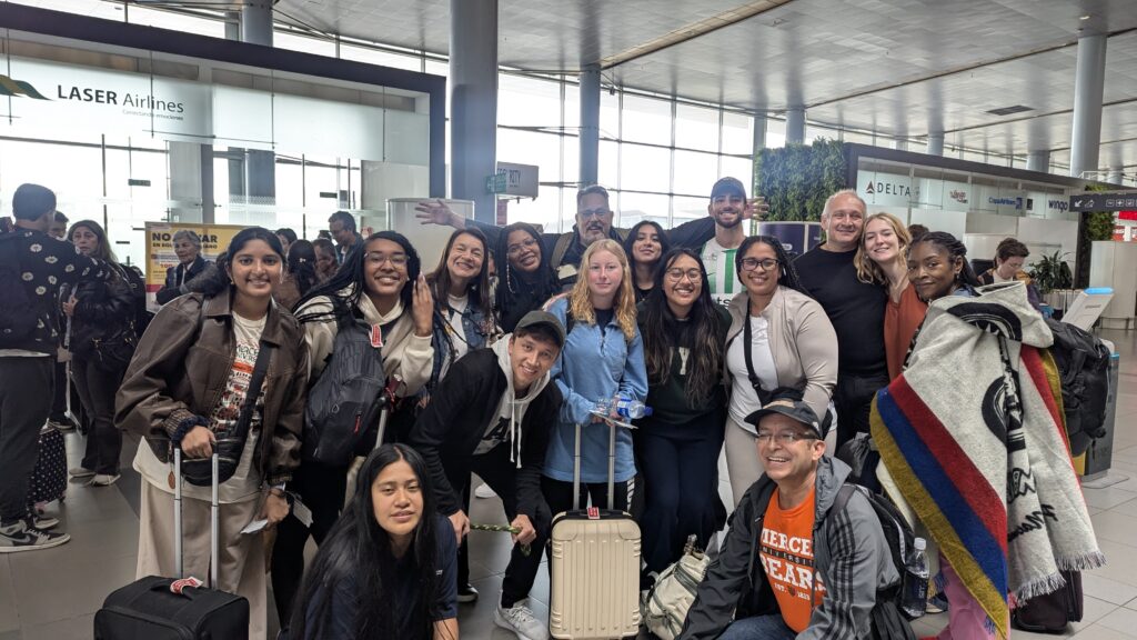 A group of people pose with luggage inside an airport terminal near airline check-in counters.