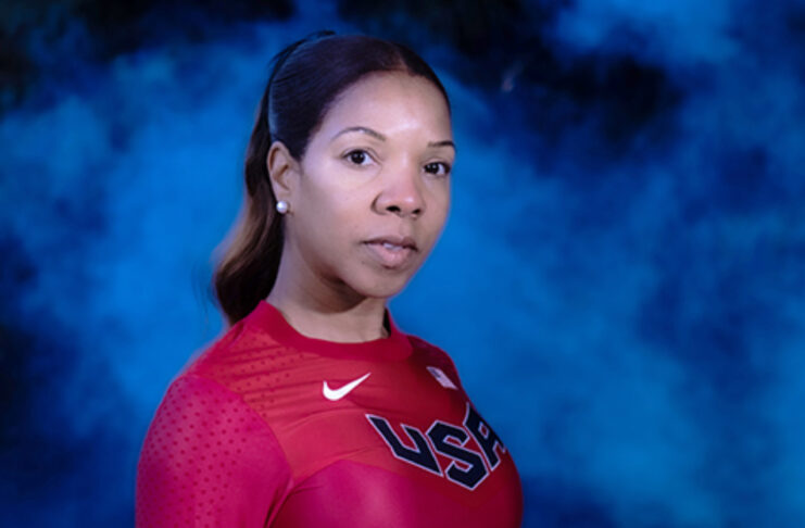 A woman in a red long-sleeve USA athletic shirt stands in front of a blue, smoky background, looking at the camera.