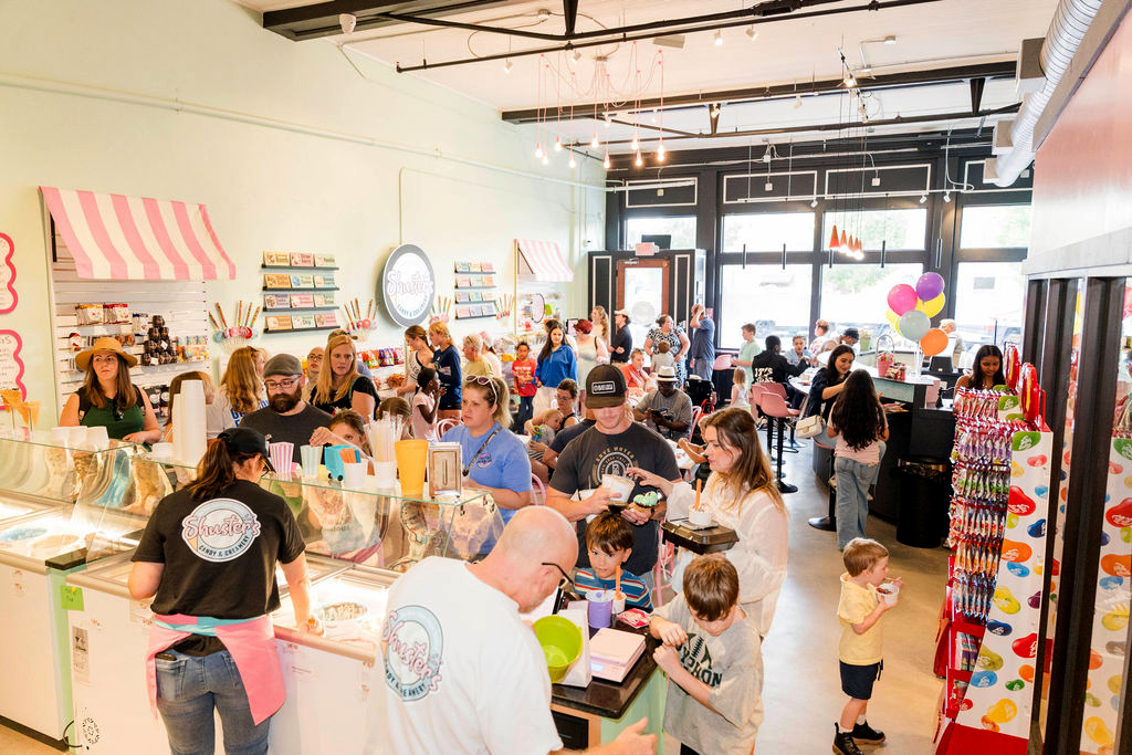 A crowded ice cream shop with adults and children ordering, eating, and socializing inside a brightly lit space.
