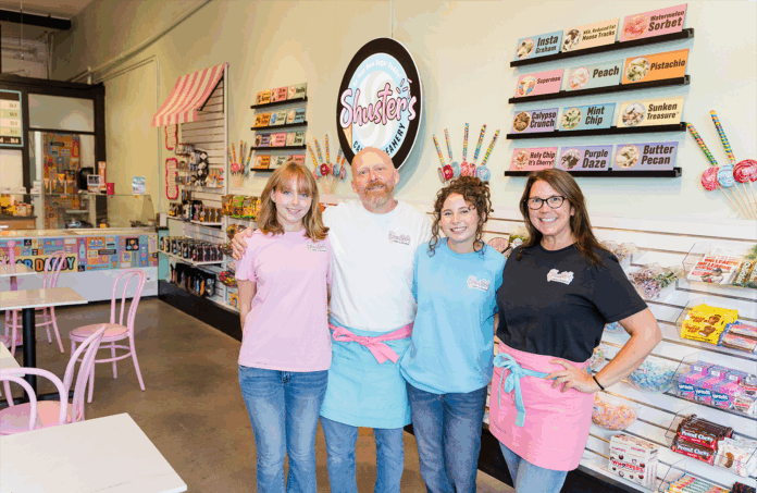 Four staff members stand together inside a colorful ice cream and candy shop, smiling at the camera.