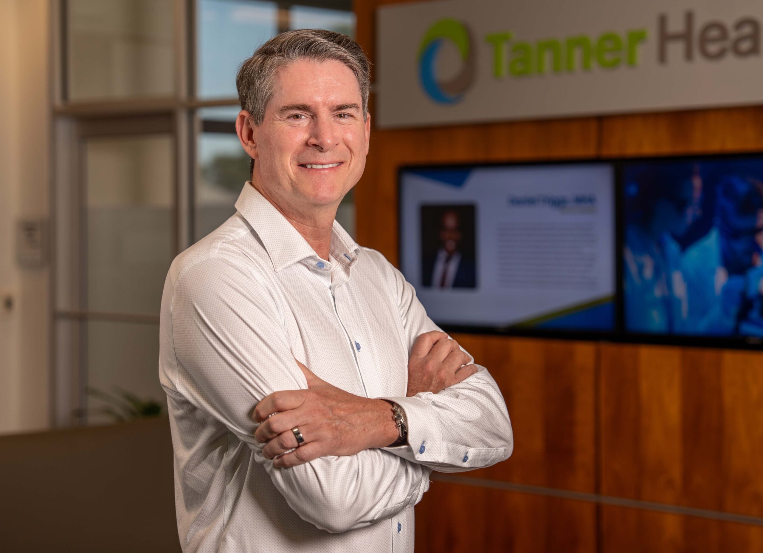Dr. Tim Paul stands with arms crossed in front of a Tanner Health sign and digital display.