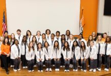 Mercer expands nursing program to Macon campus A large group of students in white coats pose and smile together in front of American and state flags indoors.