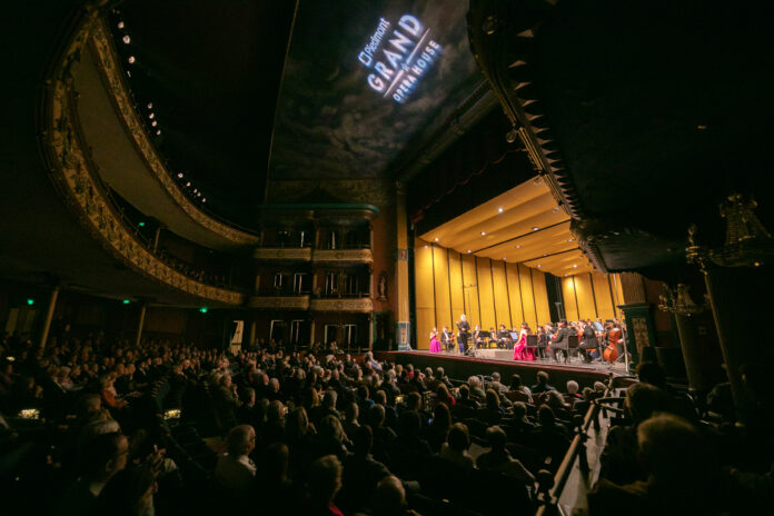 A symphony orchestra performs on stage in a grand theater filled with an attentive audience.