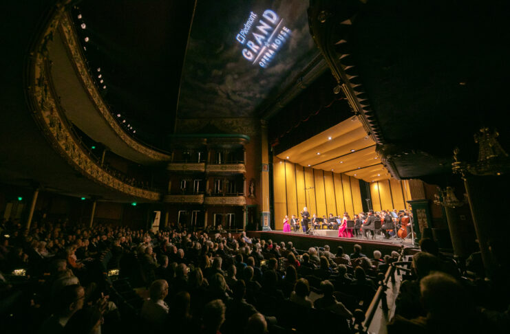 A symphony orchestra performs on stage in a grand theater filled with an attentive audience.