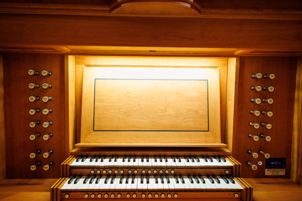 Wooden organ console with multiple rows of keys, stops on both sides, and a blank wooden music stand.