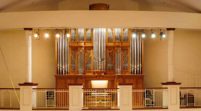 Handcrafted organ brings ‘new dimension’ to Mercer’s music programs A large pipe organ with ornate woodwork is displayed behind a railing in a well-lit concert hall.