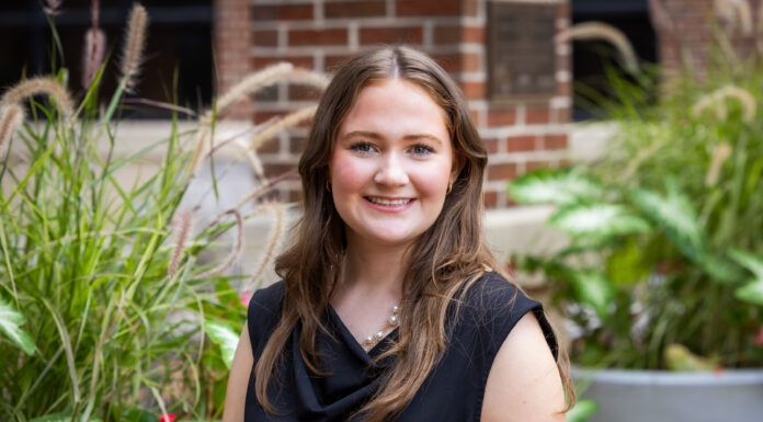 Mercer junior gains civil engineering experience in the field Young woman with long brown hair wearing a black top, smiling outdoors in front of greenery and a brick wall.