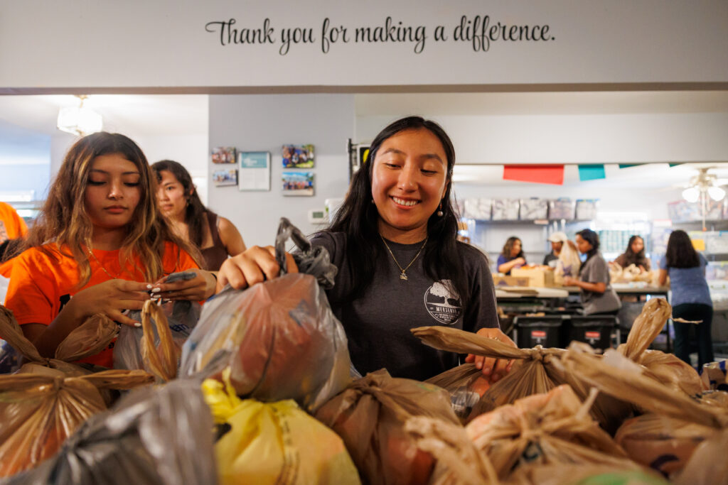 Mercer students pack grocery bags with food in a community center, with a sign reading “Thank you for making a difference.”.