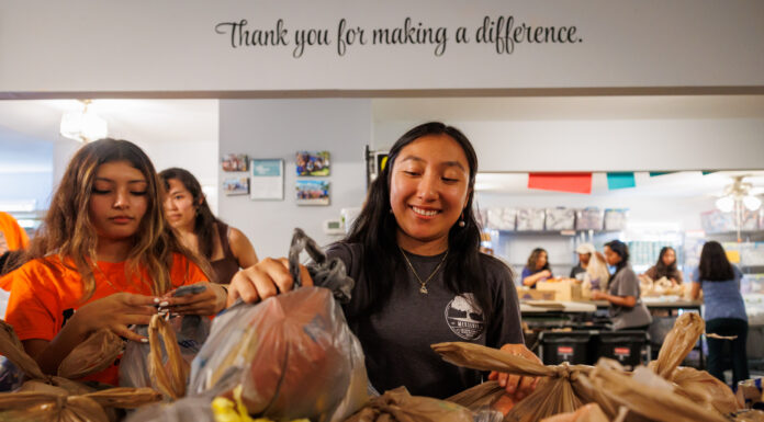 MerServe celebrates 10 years of service to community Mercer students pack grocery bags with food in a community center, with a sign reading “Thank you for making a difference.”.