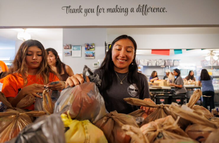 Mercer students pack grocery bags with food in a community center, with a sign reading “Thank you for making a difference.”.