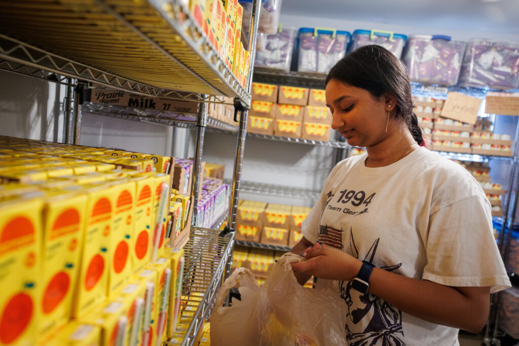 A Mercer student places juice boxes into a plastic bag in a pantry stocked with boxed goods and other supplies.