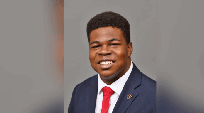 Junior Alexander Marshall chosen to receive Voyager Scholarship for Public Service A young man in a suit and red tie smiles at the camera against a plain gray background.