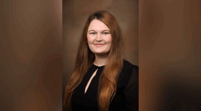 Assistant director of fellowships and scholarships selected for U.S. International Council on Disabilities Youth Advisory Committee Woman with long brown hair wearing a black top, smiling at the camera against a brown gradient background.