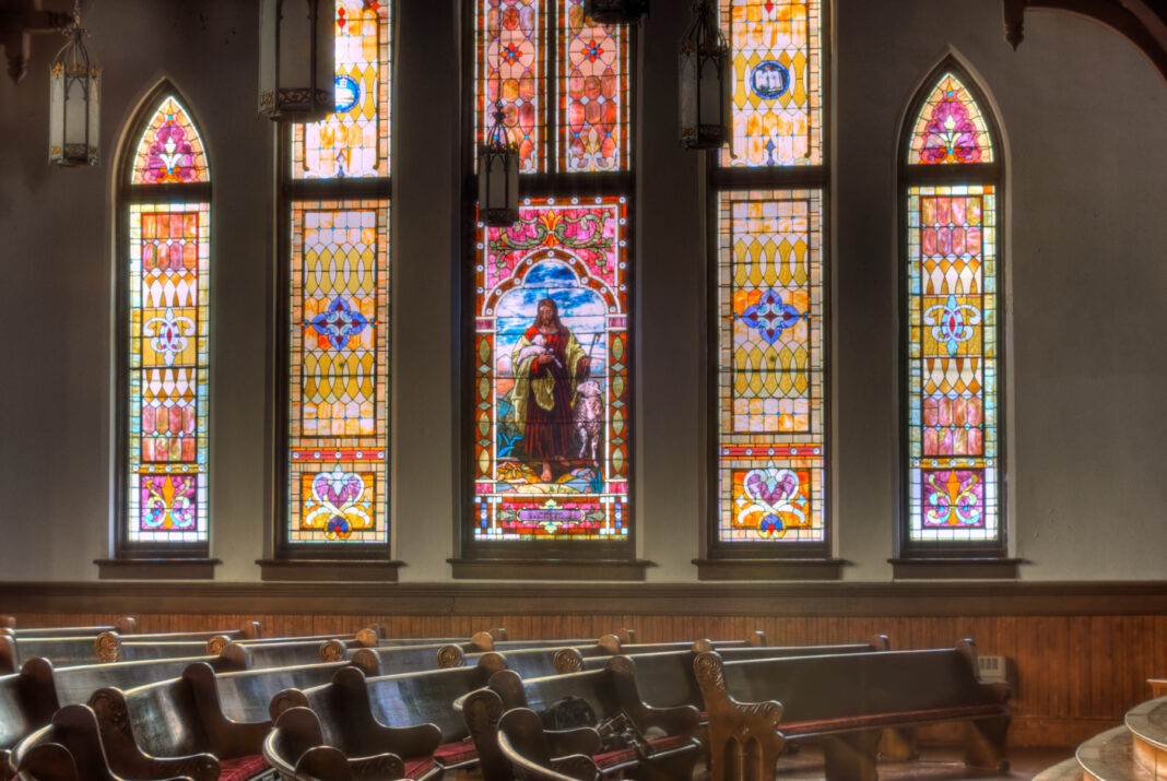 Interior of Mercer University's Newton Chapel with wooden pews and large stained glass windows featuring Jesus.