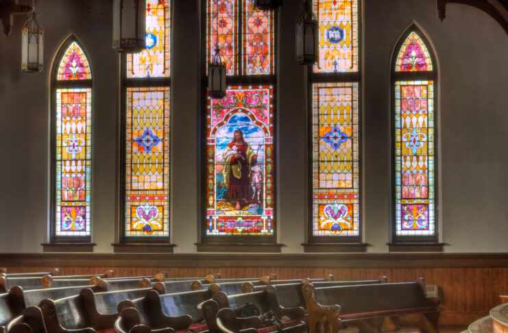 Interior of Mercer University's Newton Chapel with wooden pews and large stained glass windows featuring Jesus.