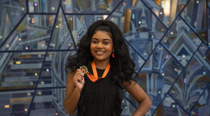 Mercer program helps freshmen grow as leaders on campus Georgia Taylor smiles while holding a medal on an orange ribbon in front of a geometric background.