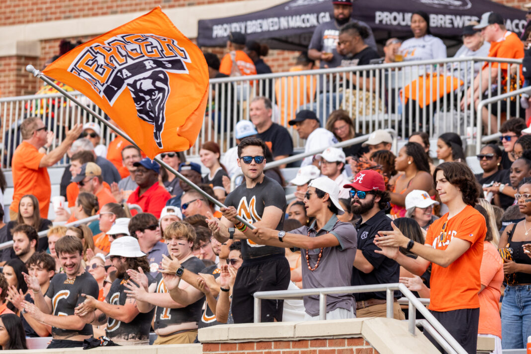 A crowd watches a football game as a man waves a Mercer University Bears flag in the stands.