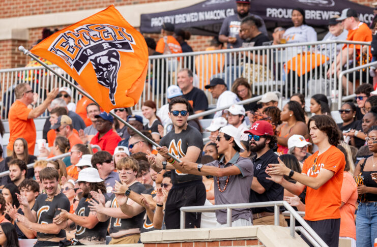 A crowd watches a football game as a man waves a Mercer University Bears flag in the stands.